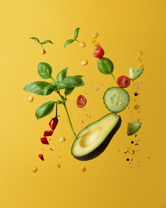Avocado, basil, corn, cucumber, and chili slices floating against a yellow background